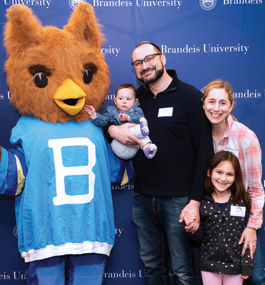 Ollie, the Brandeis mascot owl, stands with a couple and their two young daughters